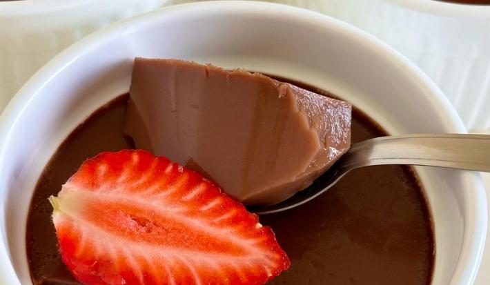 Fotografia em tons de branco com um vários potinhos brancos ao centro. Dentro dos potes existe uma receita de gelatina de chocolate finalizada com morango