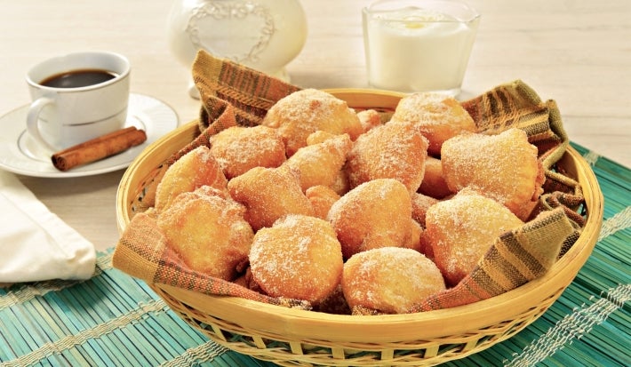 Em cima de uma mesa, cesta de palha com pano listrado com bolinhos de chuva, polvilhado com açúcar de confeiteiro.