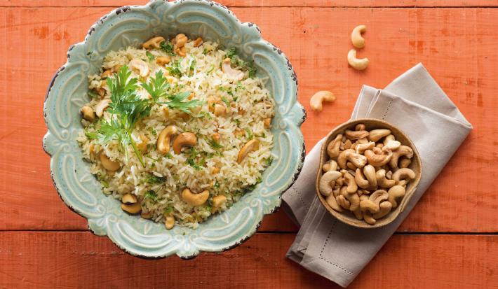 em uma mesa na cor vermelha, contém dois recipientes. Um contém o arroz e o outro as castanhas-de-caju.