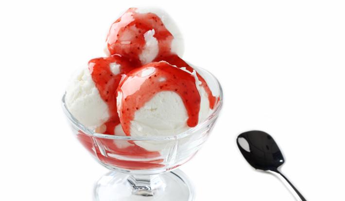 fotografia em tons de branco e vermelho tirada de uma taça de sorvete com calda de frutas vermelhas
