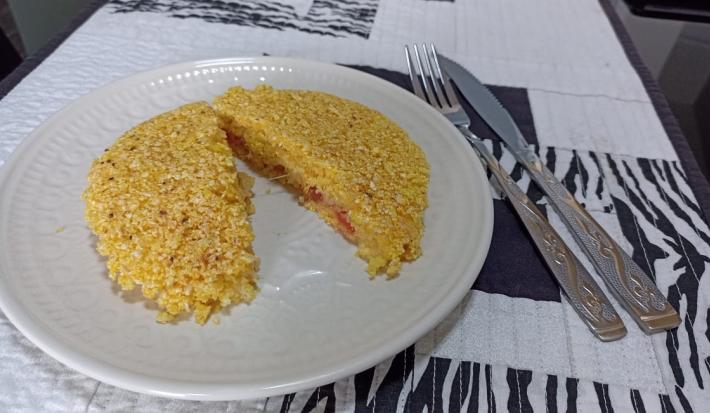 Imagem da receita de Cuscuz de frigideira recheado, sobre um prato branco e ao lado os talheres