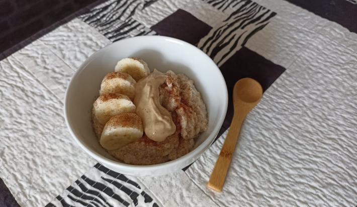 Imagem da receita de Mingau proteico pós treino, em um pote médio, sobre uma toalha e ao lado uma colher de madeira