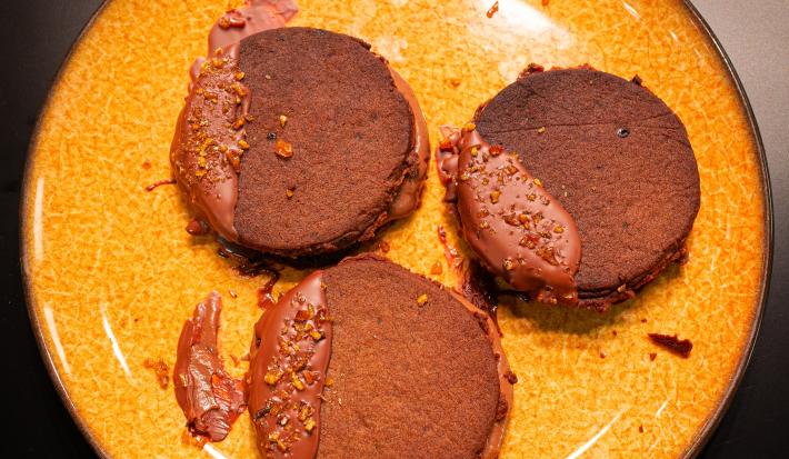 Fotografia em tons de amarelo com um prato amarelo ao centro. Em cima do prato existe uma receita de biscoito de chocolate recheado com sorvete de chocolate.
