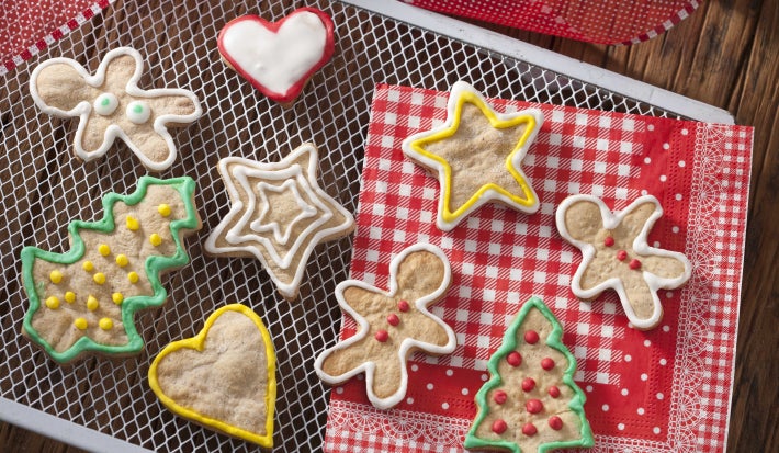 Em uma mesa de madeira, contém uma grade com vários biscoitinhos. Abaixo dessa grade contém dois panos nas cores vermelho e branco.