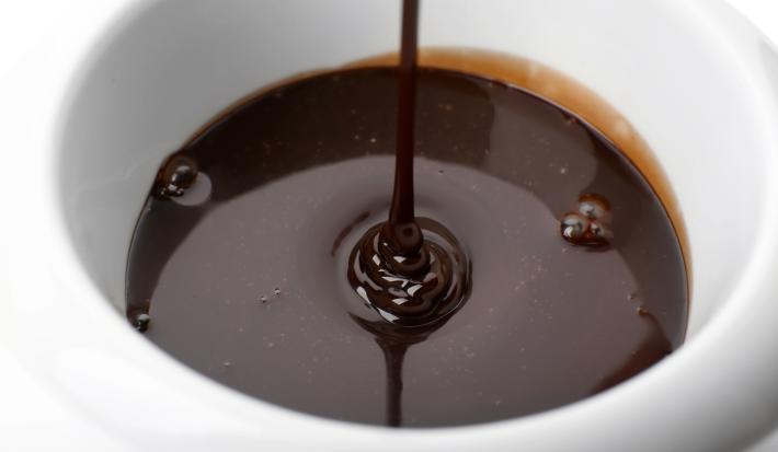 Imagem bem aproximada de um bowl branco com calda de chocolate caindo em fio.