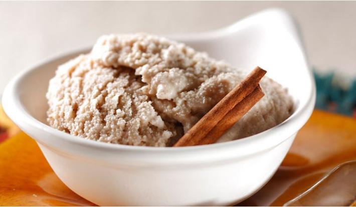 Fotografia em tons de laranja em uma mesa com toalha laranja, um potinho branco com o sorvete de canela, cravo e creme de leite.