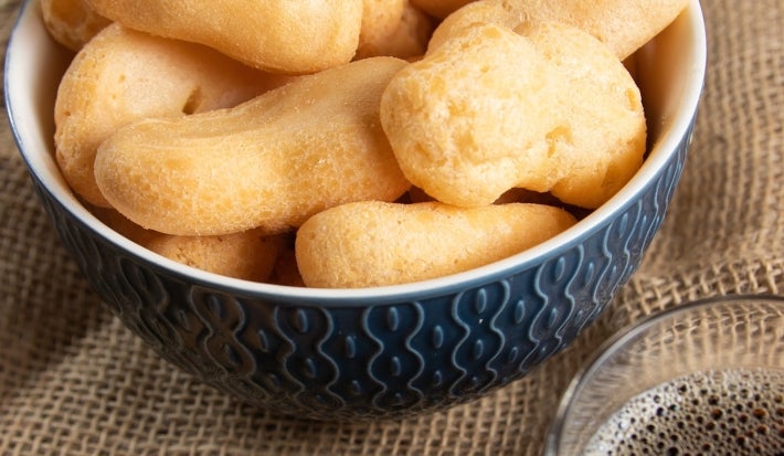 Em cima de uma mesa, tigela com biscoitos de polvilho crocantes e dourados.