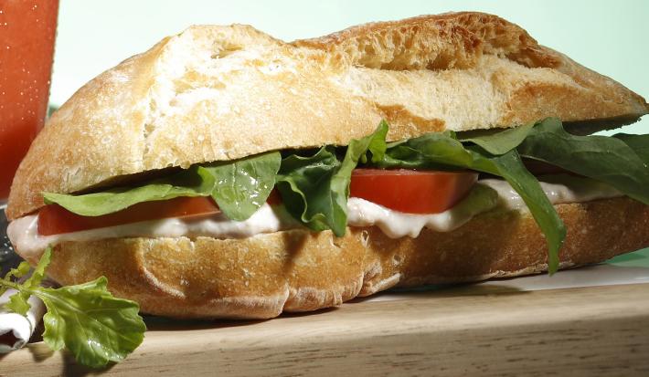 Em uma bancada contém um sanduíche recheado com patê de Requeijão Cremoso NESTLÉ e atum com rúcula e tomate
