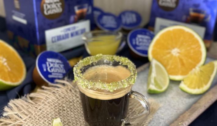Foto da receita de Café Cítrico. Observa-se uma xícara pequena de vidro com a borda açucarada e o espresso dentro. Laranjas, limões e cápsulas de NESTLÉ DOLCE GUSTO Espresso Cerrado Mineiro decoram a foto.