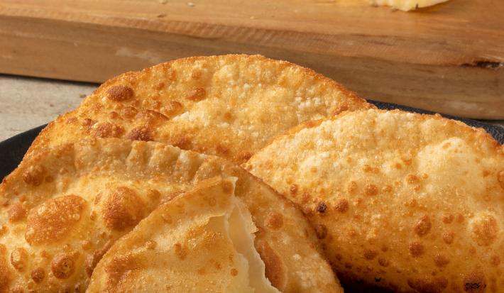 Fotografia de cinco pasteis fritos sobre um prato escuro. Um desses pasteis está aberto, mas sem recheio.