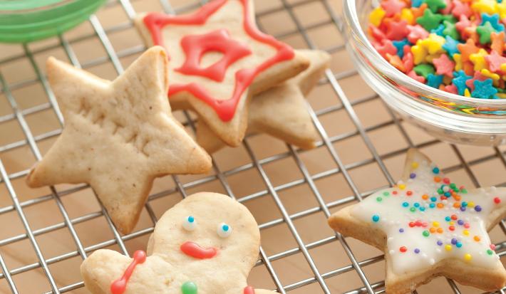 Fotografia de biscoitos decorados de natal em formato de boneco, estrela e presentes, nas cores vermelho, verde e branco, decorados com confeitos das mesmas cores.