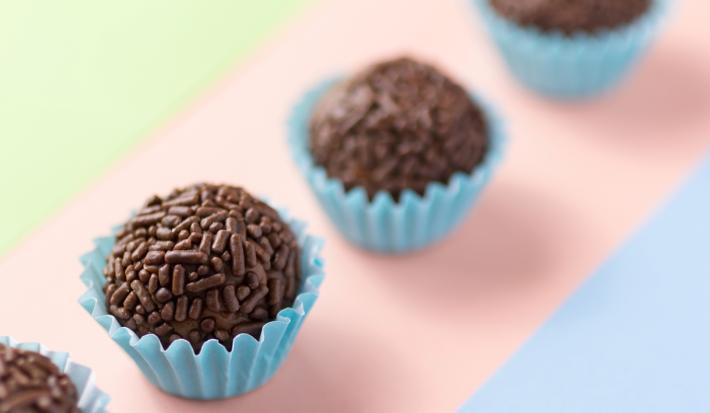 Imagem de brigadeiros enfileirados cobertos com chocolate granulado na forminha azul claro.