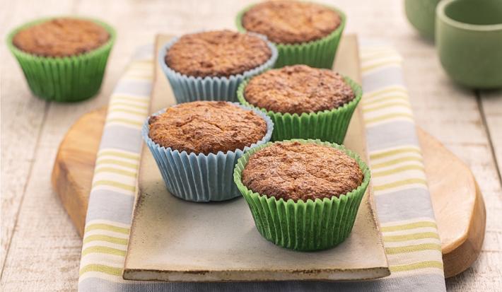 Foto da Receita de Cupcake Leve FiberMais. Observa-se uma tábua de madeira sobre um guardanapo listrado e os cupcakes em cima em forminhas verdes e azuis.