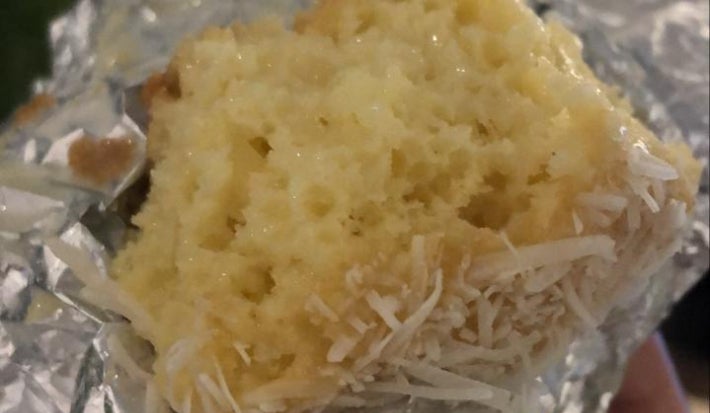 Fatia de bolo gelado de coco envolta em papel-alumínio, mostrando massa clara e textura macia.