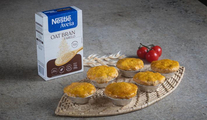 Foto aproximada da receita de empadinha de palmito, estão seis servidas na bancada, com um ramo de trigo decorando, tomates-cereja e uma caixa de nestlé farelo de aveia à esquerda