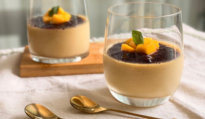 Fotografia mostra dois copos transparentes com creme alaranjado e frutas no topo.