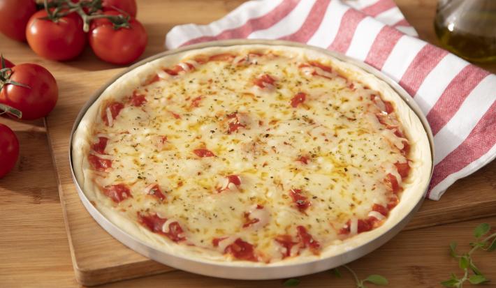 Imagem de uma pizza redonda de queijo muçarela com um paninho listrado vermelho e branco do lado e tomates.