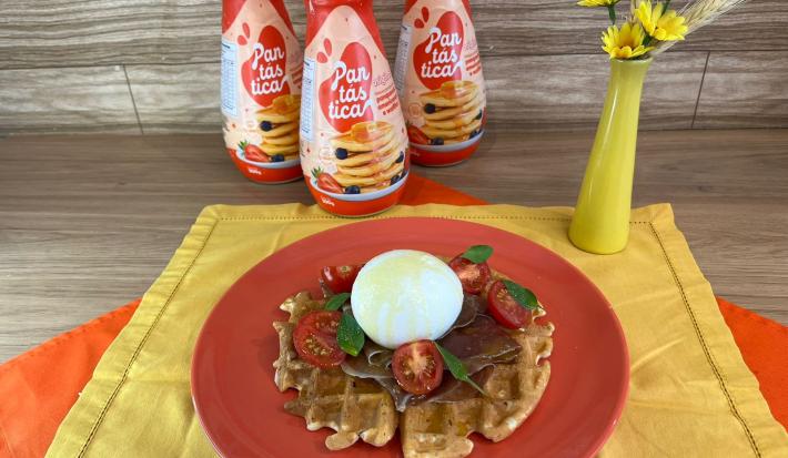 Fotografia em tons de vermelho com um prato vermelho ao centro. Em cima do prato existe uma receita de waffle com burrata, presunto de parma, tomate cereja e manjericão. Ao fundo existe três garrafas de PANTÁSTICA, um produto para fazer panquecas.