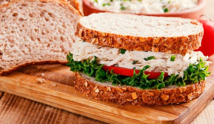 Foto da receita de Sanduíche de Salpicão de Frango. Observa-se um sanduíche bem perto expondo o recheio de frango cremoso com a salada de alface e tomate embaixo.