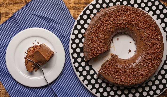 Imagem de um brigadeirão coberto com chocolate granulado e uma fatia em um prato branco.