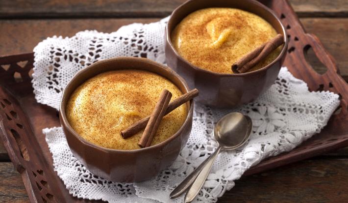Foto de uma bandeja marrom com uma toalha branca em cima e 2 potes marrons com curau dentro e canela decorando