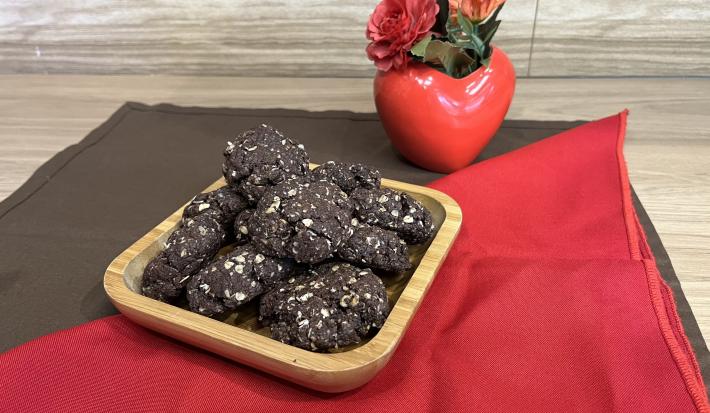 Fotografia em tons de vermelho e marrom com um recipiente de madeira ao centro. Dentro do recipiente existe vários cookies de NESCAU com NESTLÉ Aveia Flocos!