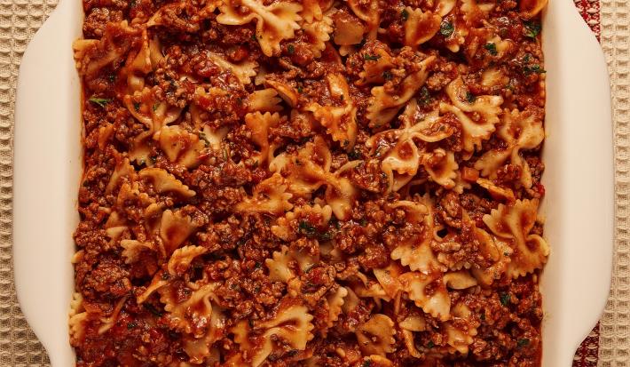 Foto bem aproximada de uma travessa branca com a receita de macarrão tipo gravatinha com molho bolonhesa