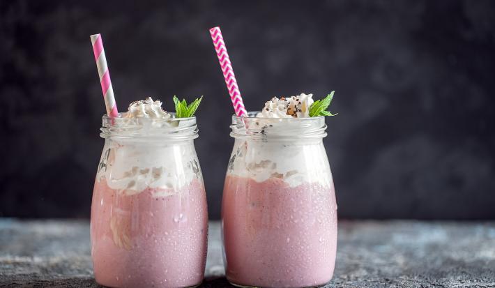 Fotografia de dois recipientes decorativos de vidro com frapê com Leite MOÇA, guaraná e suco de limão. No mesmo copo tem um canudo rosa e branco e hortelã.