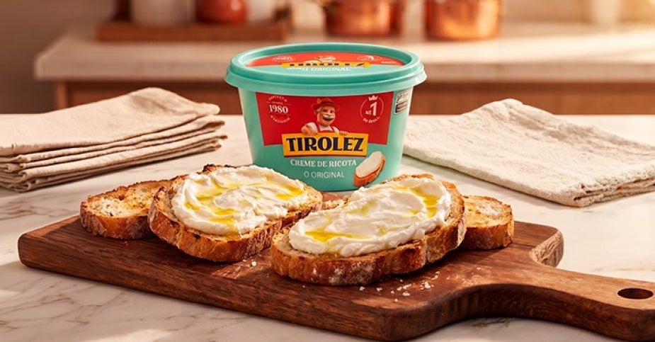 Pote de creme de ricota Tirolez com pão artesanal e creme de ricota espalhado sobre tábua de madeira	