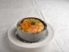 Em cima de uma mesa, prato de porcelana cinza com queijo gratinado, decorado com folha de salsa.