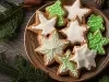 Em cima de uma mesa, prato redondo com porção de biscoitos em forma de estrela, decorados com glacê branco e verde.