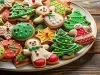 Em cima de uma mesa, prato com biscoitos em formato de árvores de Natal, bonecos de neve e biscoito redondos, decorados com glacê colorido e confeitos coloridos de bolinhas verde e vermelho.