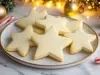 Em cima de uma mesa decoradas enfeites de natal, prato com biscoitos em formato de estrelas.