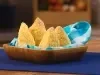 Fotografia de uma bancada de madeira com um pano azul escuro. Sobre ele tem um recipiente quadrado de madeira com um pano azul e branco forrando as quatro coxinhas saudáveis que estão dentro.