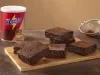 Foto da receita de brownie com nescau extra cacau servida em diversas porções sobre uma tábua de madeira, que acompanha uma peneira e uma embalagem de nescau ao fundo em cima de uma mesa de mármore escuro Foto da receita de brownie com nescau extra cacau servida em diversas porções sobre uma tábua de madeira, que acompanha uma peneira e uma embalagem de nescau ao fundo em cima de uma mesa de mármore escuro