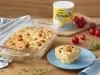 Fotografia em tons de azul de uma bancada de madeira com uma travessa de vidro com a torta cremoso, ao lado um pratinho azul com uma fatia de torta e ao fundo uma lata de NINHO Levinho e tomatinhos cereja.