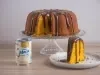 Foto da receita de Bolo de Cenoura com Cobertura de Brigadeiro, servido em um prato alto de vidro, com um pedaço cortado ao lado e, do lado esquerdo, uma lata de Leite Moça