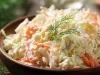 Em cima de uma mesa,  tigela com salada de maionese cremosa e colorida com cenouras raladas e repolho ralado, decoradas com folha verde.