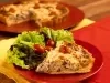 Fotografia mostra um pedaço de quiche cortada sobre um prato vermelho, ao lado folhas verdes de alface e tomate cereja.