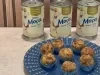 Docinhos cobertos com lascas de coco tostado em forminhas azuis, servidos em prato azul com Leite Moça ao fundo.