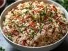 Em cima de uma mesa, tigela branca com arroz soltinho, bacon picado em pedaços, decorado com salsinha picada.