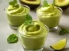 Imagem de três potinhos de vidro com a receita de mousse de abacate decorados com uma folha de hortelã.