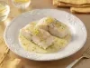 Filés de bacalhau servidos com molho cremoso de ervas e raspas de limão, apresentados em prato branco elegante.