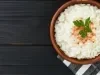 Em cima de uma mesa, tigela marrom com arroz doce cremoso, decorado com canela em pó e uma folha de salsinha.