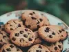 Em cima de uma mesa, prato redondo com biscoitos crocantes com gotas de chocolate.
