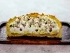 Em cima de uma mesa, banoffee cortada ao meio com massa de biscoitos crocante, bananas em rodelas, doce de leite, decorado com chantilly e canela em pó.