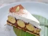 Em cima de uma mesa, prato com fatia de banoffee com massa crocante, doce de leite cremoso e bananas em rodelas, decorado com chantilly e chocolate em pó.