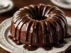 Fotografia de um bolo de chocolate em forma de bundt, coberto com um rico glacê de chocolate, apresentado em um prato decorativo.