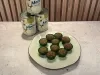 Prato com docinhos cobertos com crocante em forminhas verdes e latas de Leite Moça ao fundo.