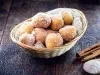 Em cima de uma mesa, cesta de palha com pano branco com bolinhos de chuva, polvilhado com açúcar de confeiteiro.